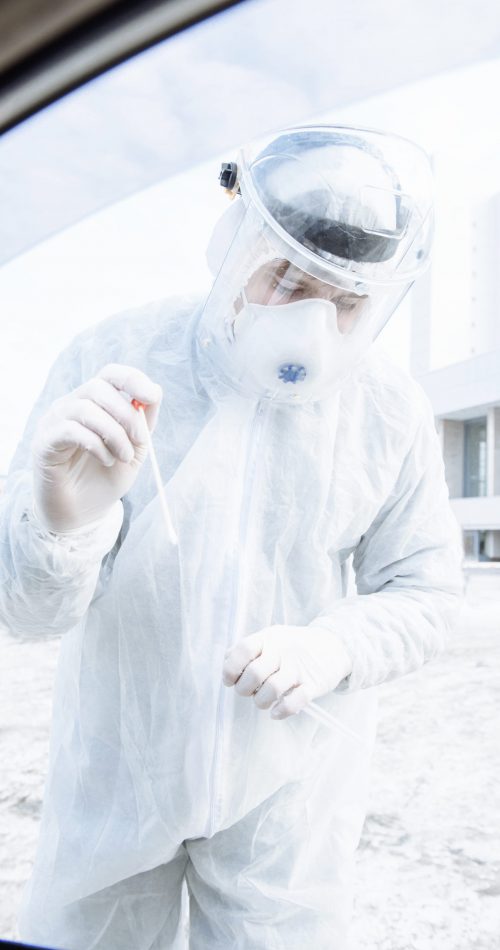 a medical worker in a protective suit PPE Hazmat takes tests for the covid-19 coronavirus virus from drivers in their car
